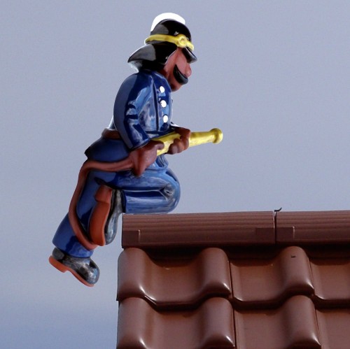 Feuerwehrmann knieend auf einem Dachziegel, traditionell mit wasserschlauch